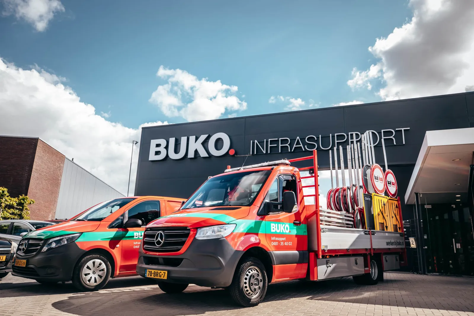 Bedrijfswagens van BUKO Infrasupport met verkeersborden voor hun pand